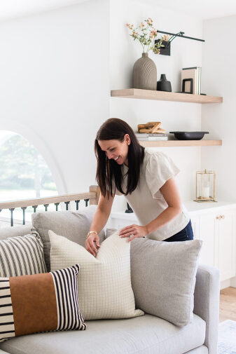 Interior stylist fluffing two throw pillows on a couch.